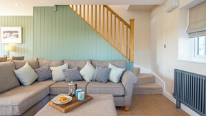 A living room with a sectional sofa, a wooden staircase, and a radiator. - Bwthyn Clyd, Holiday Cottage Llanrhian, Sleeps 4, 2 bedrooms,  bathrooms (Haverfordwest)