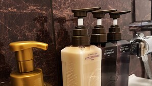 A bathroom with a marble wall, a gold-colored shower pump, and three bottles of body care products. - Nplus HOTEL Tokyo Nihonbashi (Tokyo)