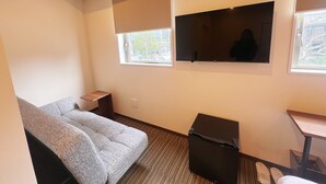 A compact hotel room with a grey sofa, a small table, a TV mounted on the wall, and a window with blinds. - Nplus HOTEL Tokyo Nihonbashi (Tokyo)