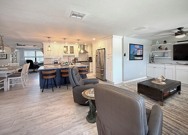 A spacious living room with a large dark coffee table, a comfortable sofa, and a dining area with a kitchen in the background.