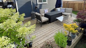 Een terras met buitenmeubilair, plantenpotten en een huis op de achtergrond.