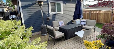 A deck with outdoor furniture, potted plants, and a house in the background.