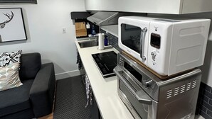 Een moderne keuken met een inbouwoven, magnetron en koffieapparaat. Er is een zwart aanrecht, een grijze bank en een zwart vloerkleed.