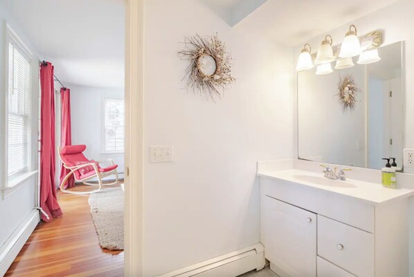 A bathroom with a white vanity, a mirror with three lights, and a decorative wreath on the wall.