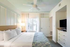 Una camera d'albergo con un letto, una ventola a soffitto, una TV, un comò e una finestra con tende.