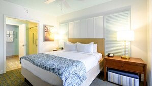 A hotel room with a bed, bedside lamps, a nightstand, a ceiling fan, and a door leading to a bathroom. - Orlando | Family Splash Stay | Pool + Waterpark | 2BR Condo (Orlando)