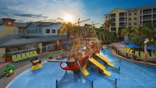 Un parque acuático con una piscina grande, toboganes y una estructura de juegos con forma de barco pirata.