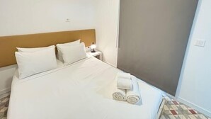 Habitación de hotel con una cama grande, dos almohadas, una mesita de noche con lámpara y una ventana con vistas.