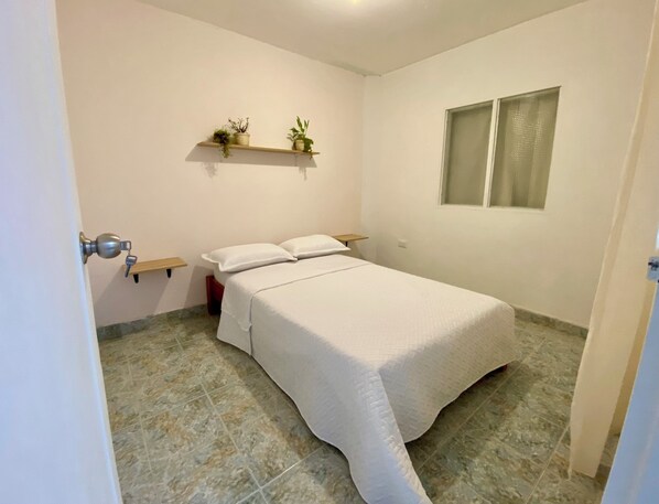 Un dormitorio con cama, una ventana y una estantería con plantas.