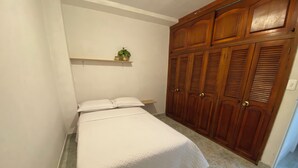 A bedroom with a bed, a wooden wardrobe, and a small shelf with a plant. - Encantadora Casa en el Corazón de Guatapé, Perfecta Para Familias y Grupos! (Guatape)