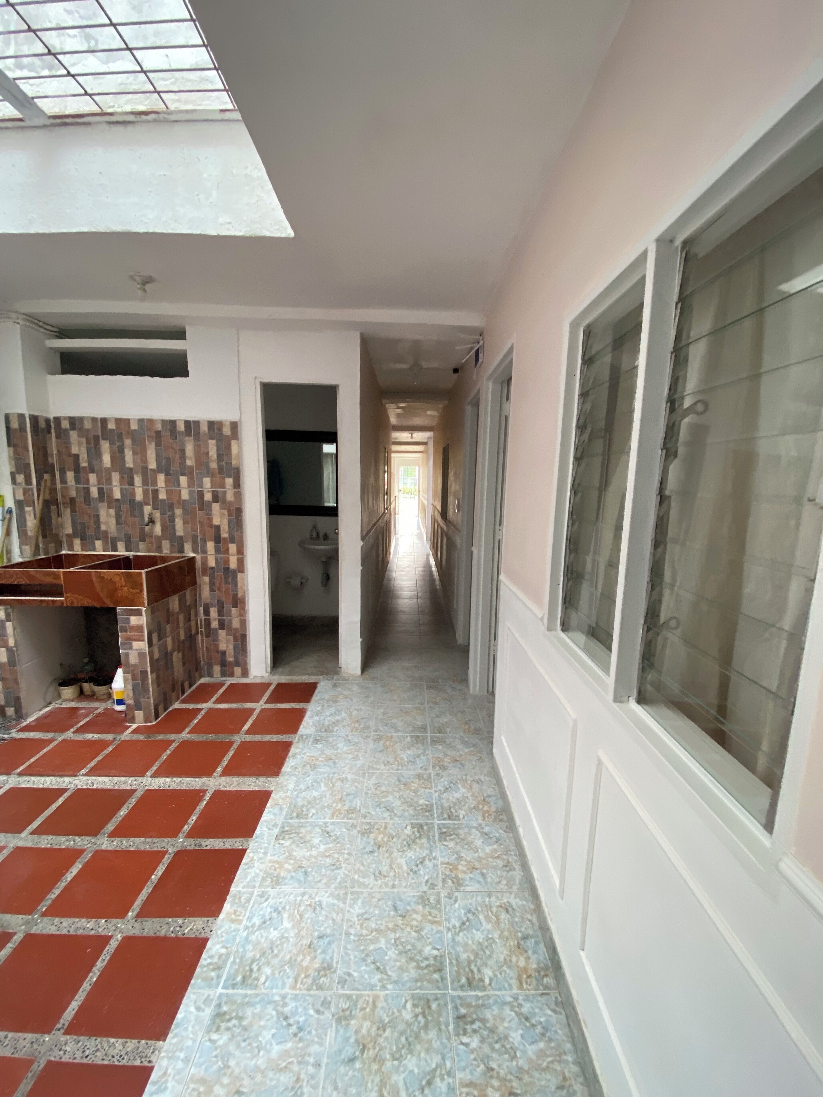 A corridor with a tiled floor, a kitchen area with a tiled backsplash, and a window with frosted glass.