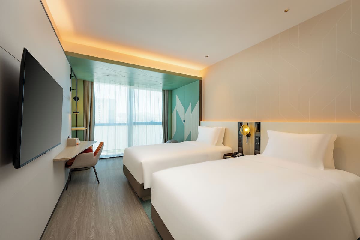 Habitación de hotel con dos camas, un escritorio, una silla, un televisor y una ventana con cortinas.