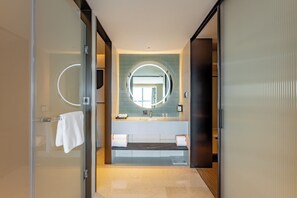 A modern bathroom with a glass door, a round mirror, a sink, and a bench.