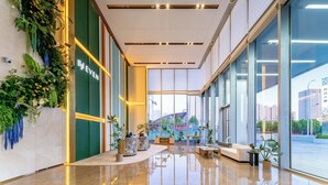 Eine moderne Lobby mit grüner Wand, einer Rezeption und einer Sitzecke mit Blick auf die Stadt.