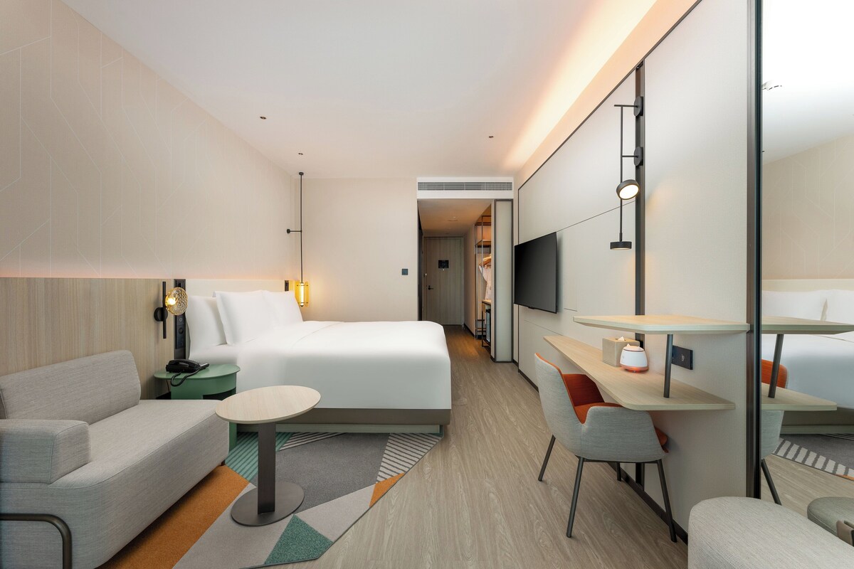 Une chambre d’hôtel moderne équipée d’un lit, d’un canapé, d’un bureau avec une chaise, d’une télévision et d’une petite table.
