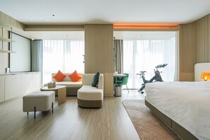 A modern hotel room with a large bed, a sofa, a small table, and a bicycle in the background.