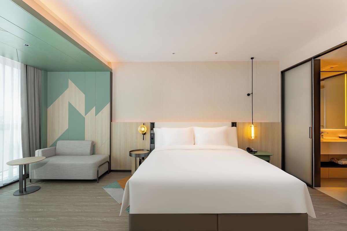 Una habitación de hotel moderna con una cama grande, zona de estar, escritorio y armario.