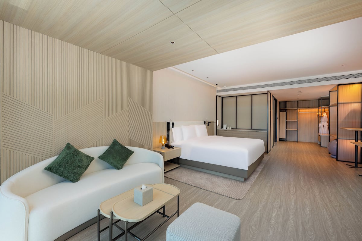 Una habitación de hotel moderna con un sofá, una cama, una mesita de noche y una pequeña mesa.