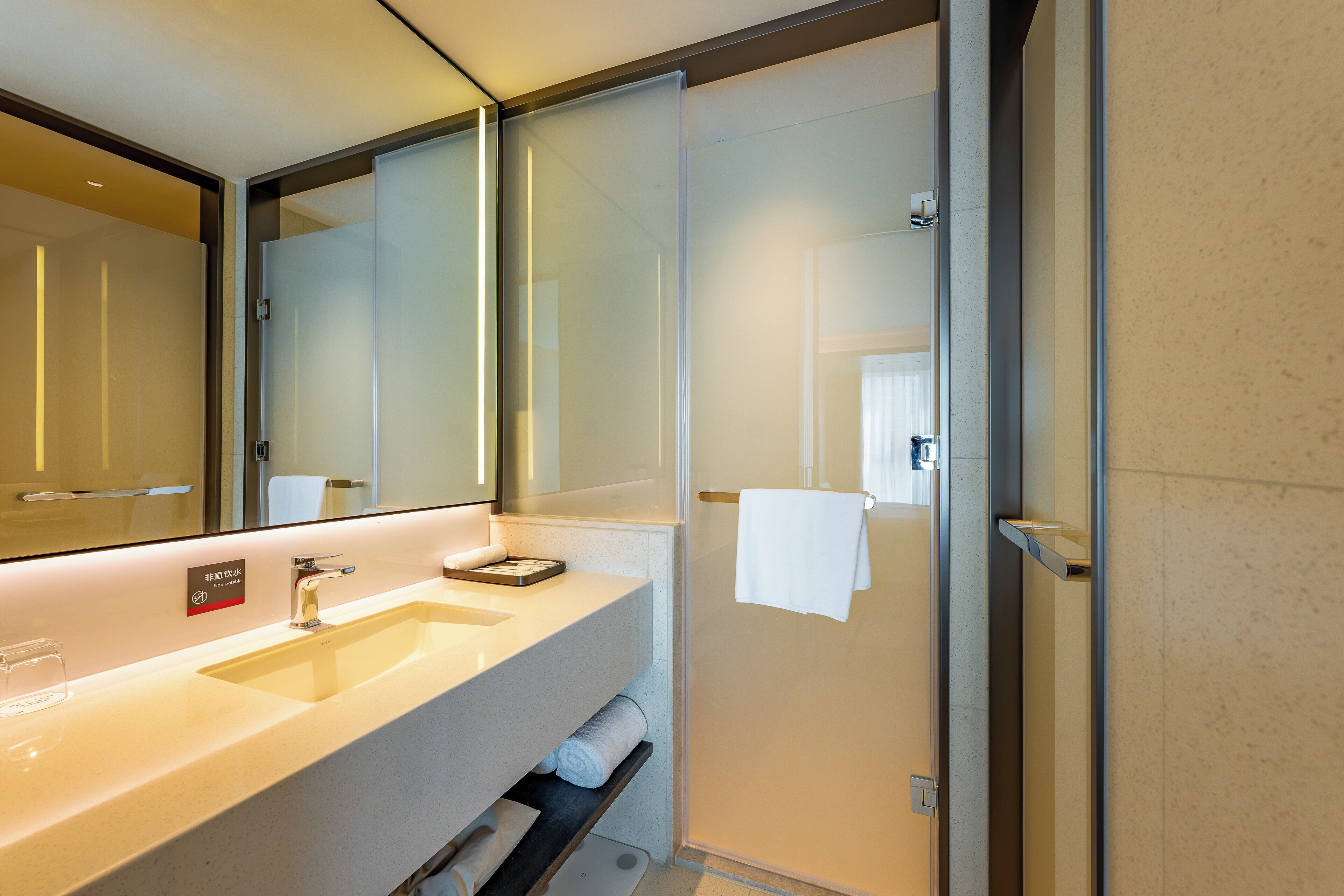 Un baño moderno con un espejo grande, dos lavamanos, un perchero para toallas y una mampara de vidrio.