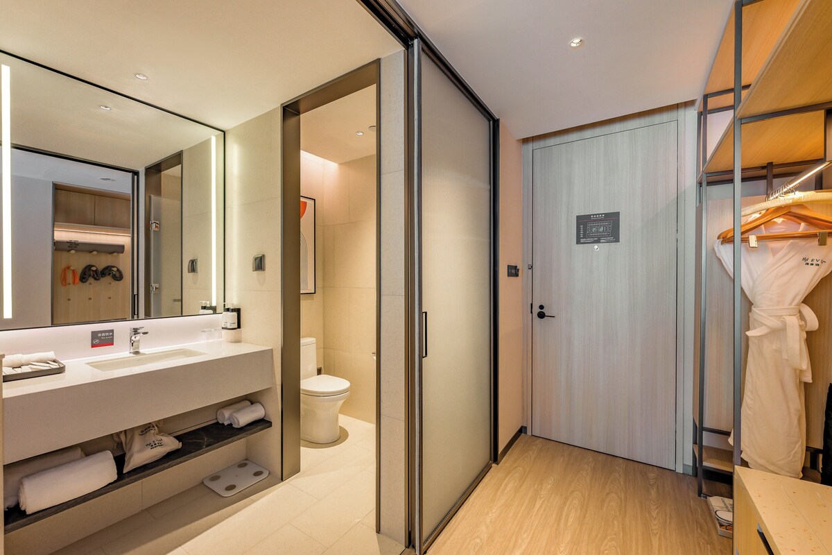 Une salle de bain moderne avec un grand miroir, un lavabo et des toilettes. Une robe est suspendue à un porte-manteau et le sol est en bois.