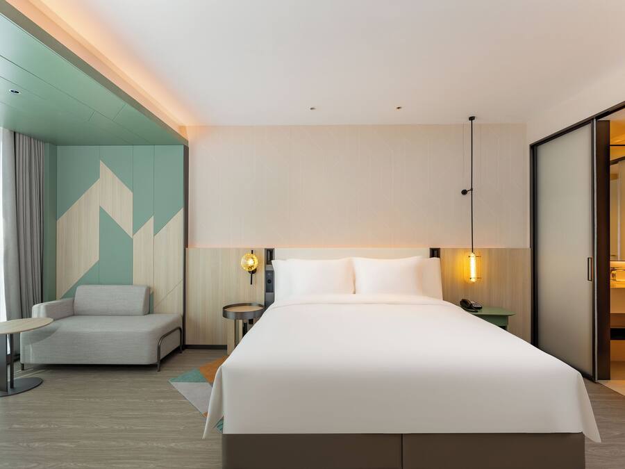A modern hotel room with a large bed, a seating area, a desk, and a bathroom.