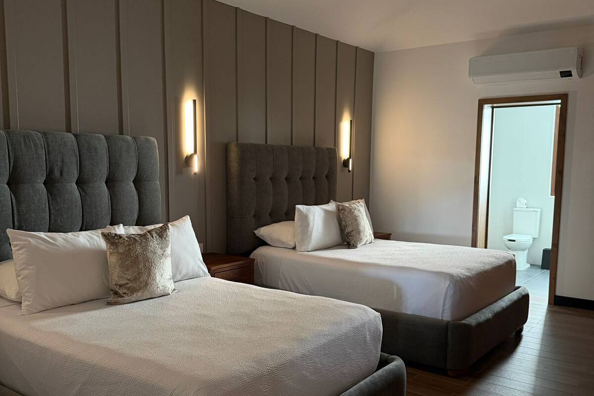 A modern hotel room with two beds, a large wall panel, and a visible bathroom.