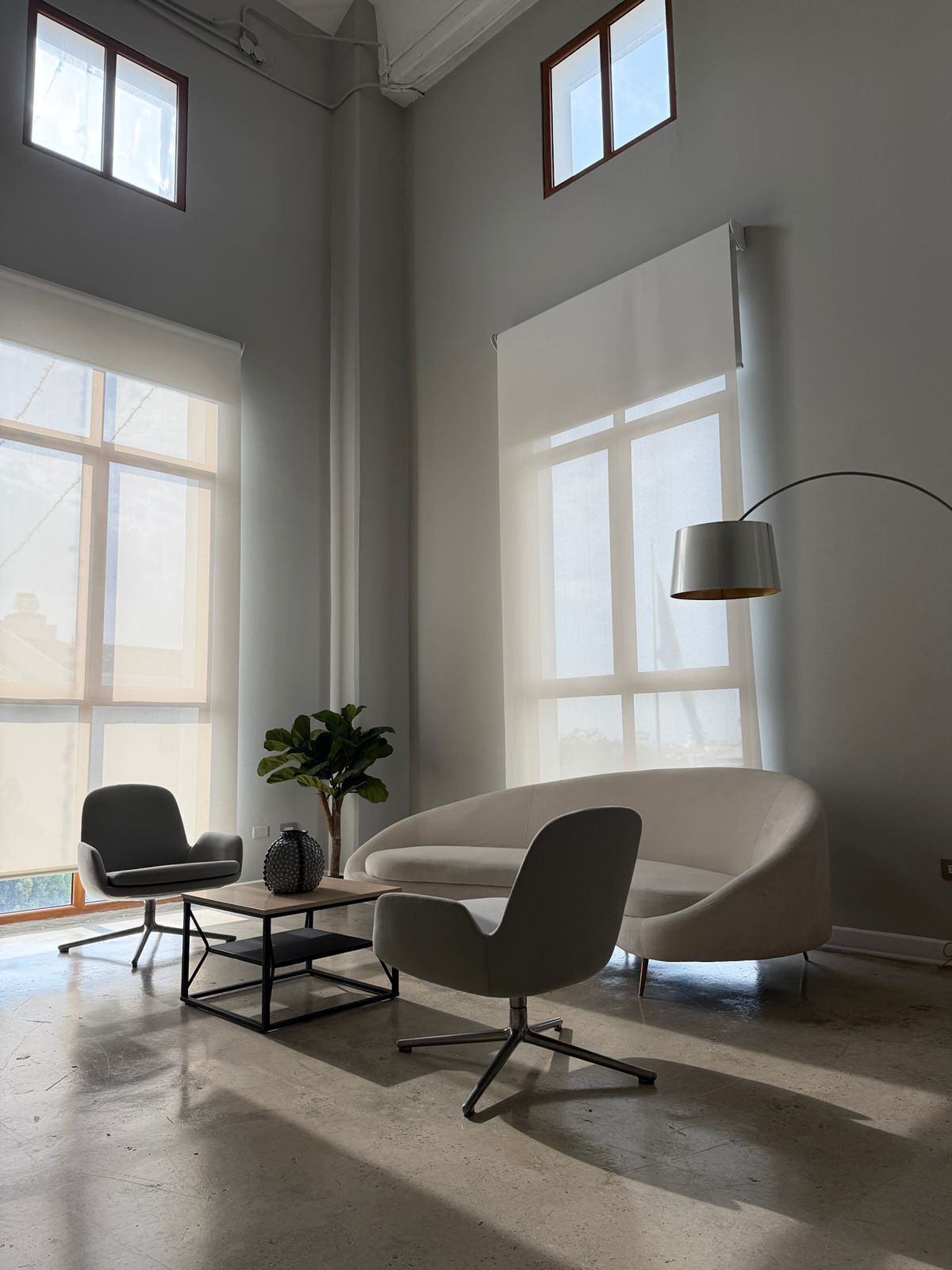 Una habitación amplia con un gran ventanal, un sofá moderno, dos sillones, una mesita y una lámpara de pie.