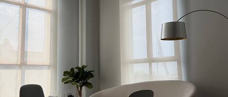 Una habitación amplia con un gran ventanal, un sofá moderno, dos sillones, una mesita y una lámpara de pie.