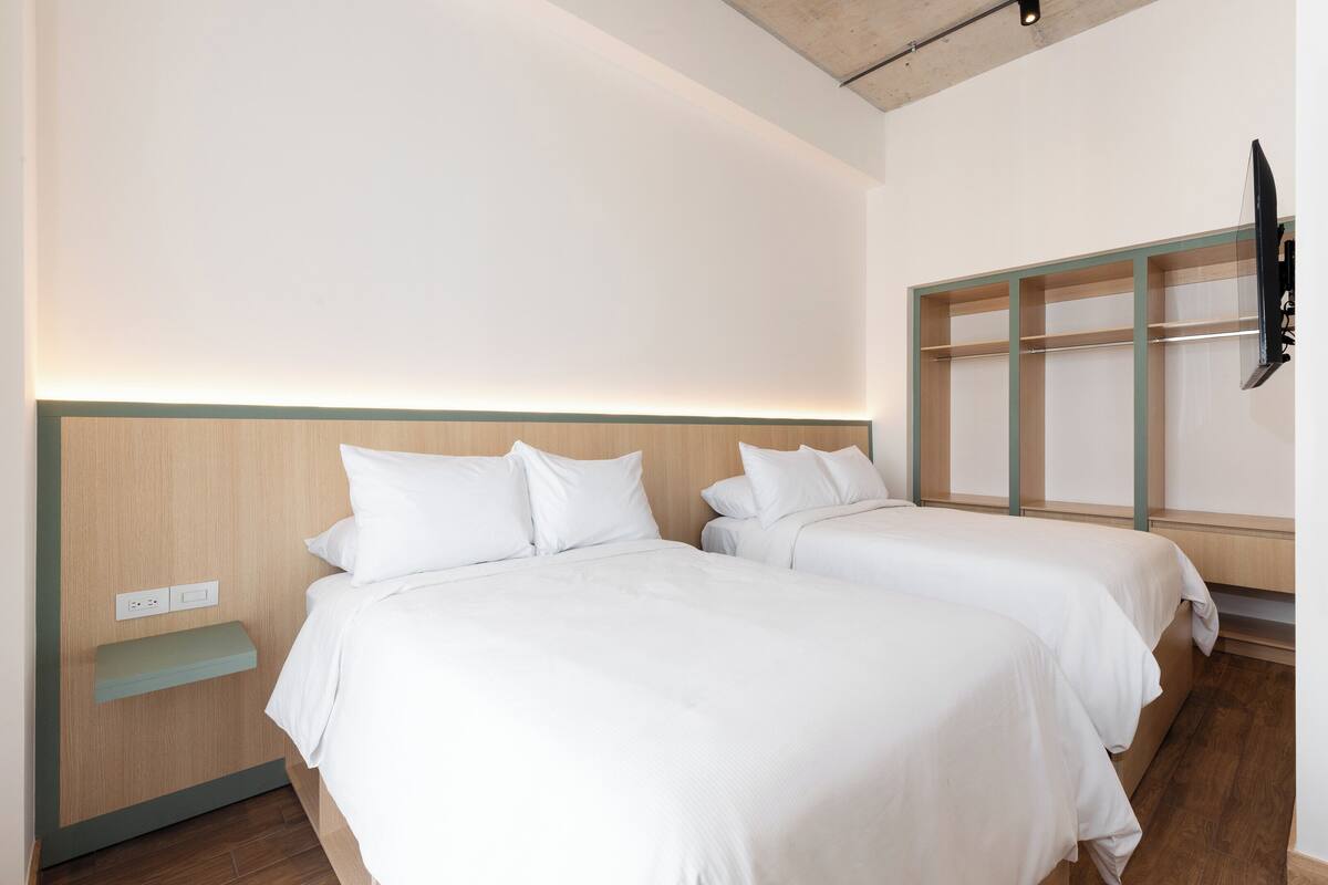 A hotel room with two beds, a wooden headboard, a small shelf, and a TV mounted on the wall.