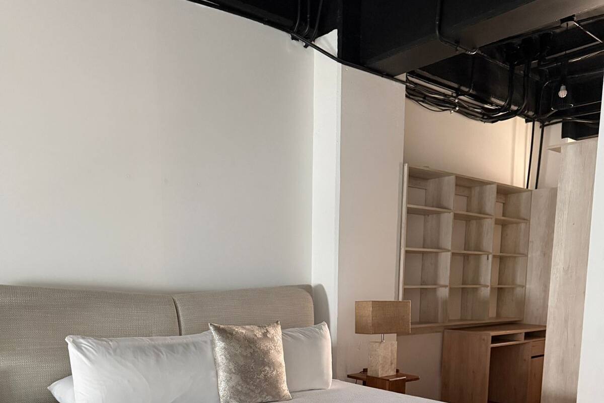 A modern bedroom with a large bed, a nightstand, a lamp, and a built-in wooden shelving unit.
