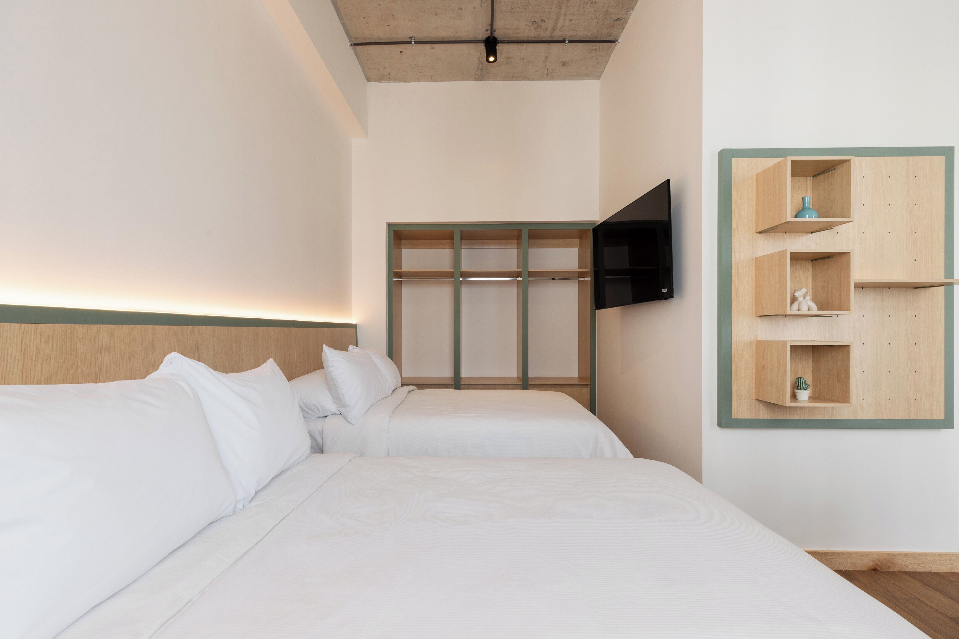 Habitación de hotel con dos camas, un televisor de pantalla plana en la pared y un estante de madera con objetos decorativos.