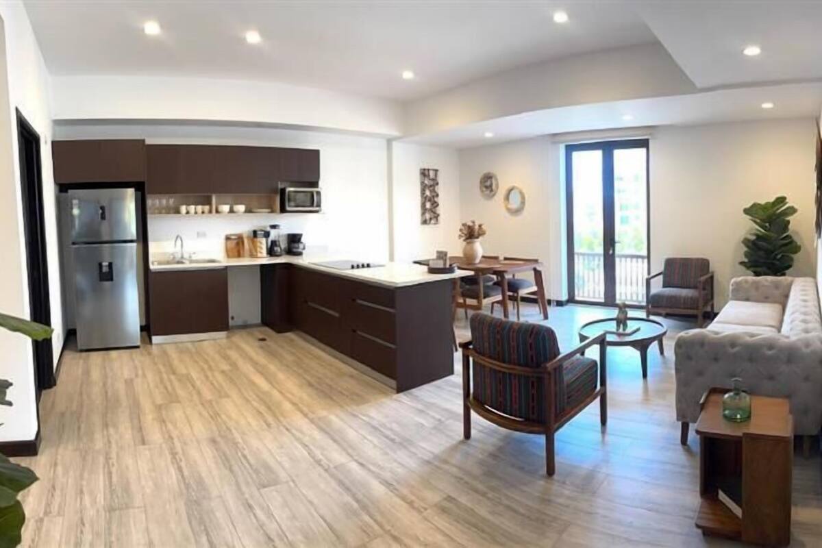 A modern kitchen with a built-in microwave, a refrigerator, and a coffee machine. There is a dining area with a round table and chairs.