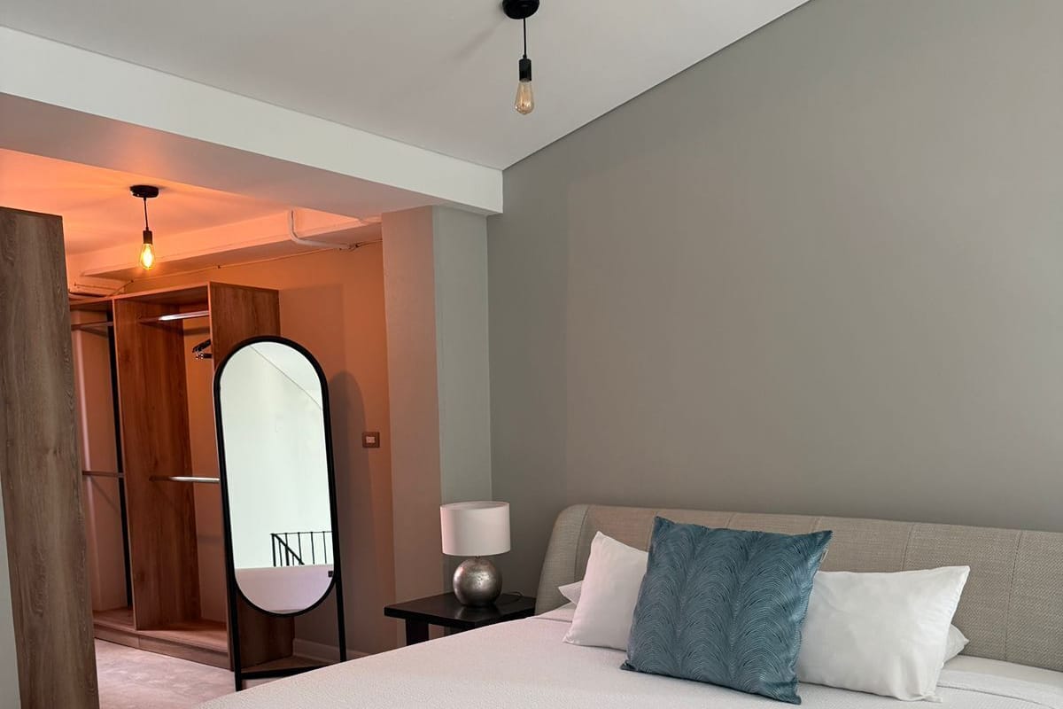 A modern bedroom with a large bed, a bedside table, a mirror, and a wooden closet.