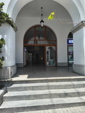 Entrada de um edifício com um arco grande, um lustre pendurado e uma escadaria.