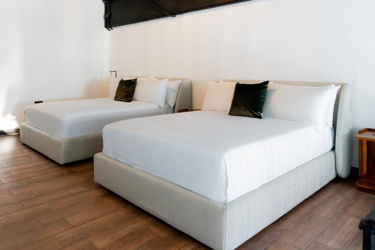 A hotel room with two beds, a wooden floor, and a small wooden side table.