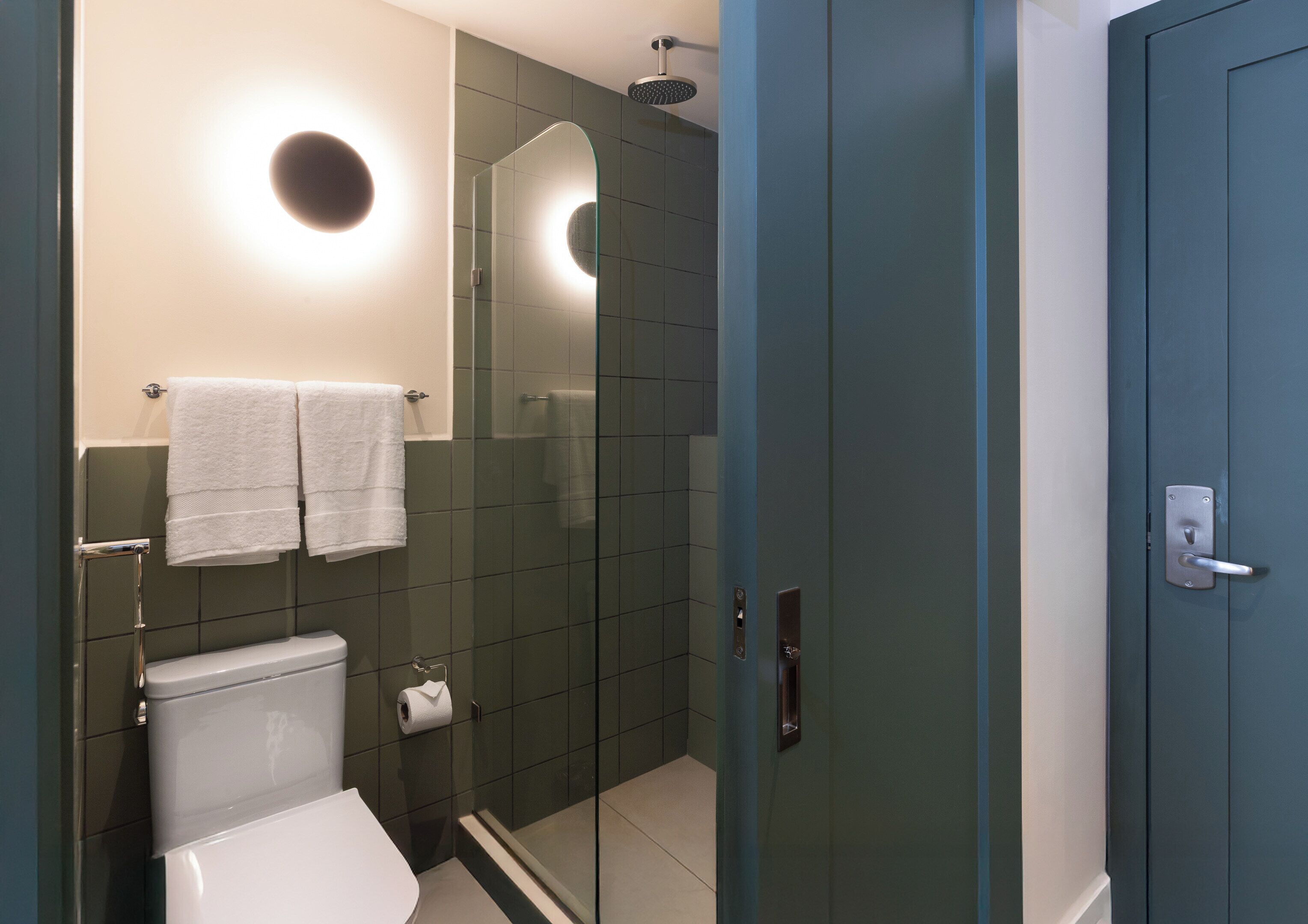 Un baño moderno con inodoro, cabina de ducha de vidrio y un perchero con dos toallas.