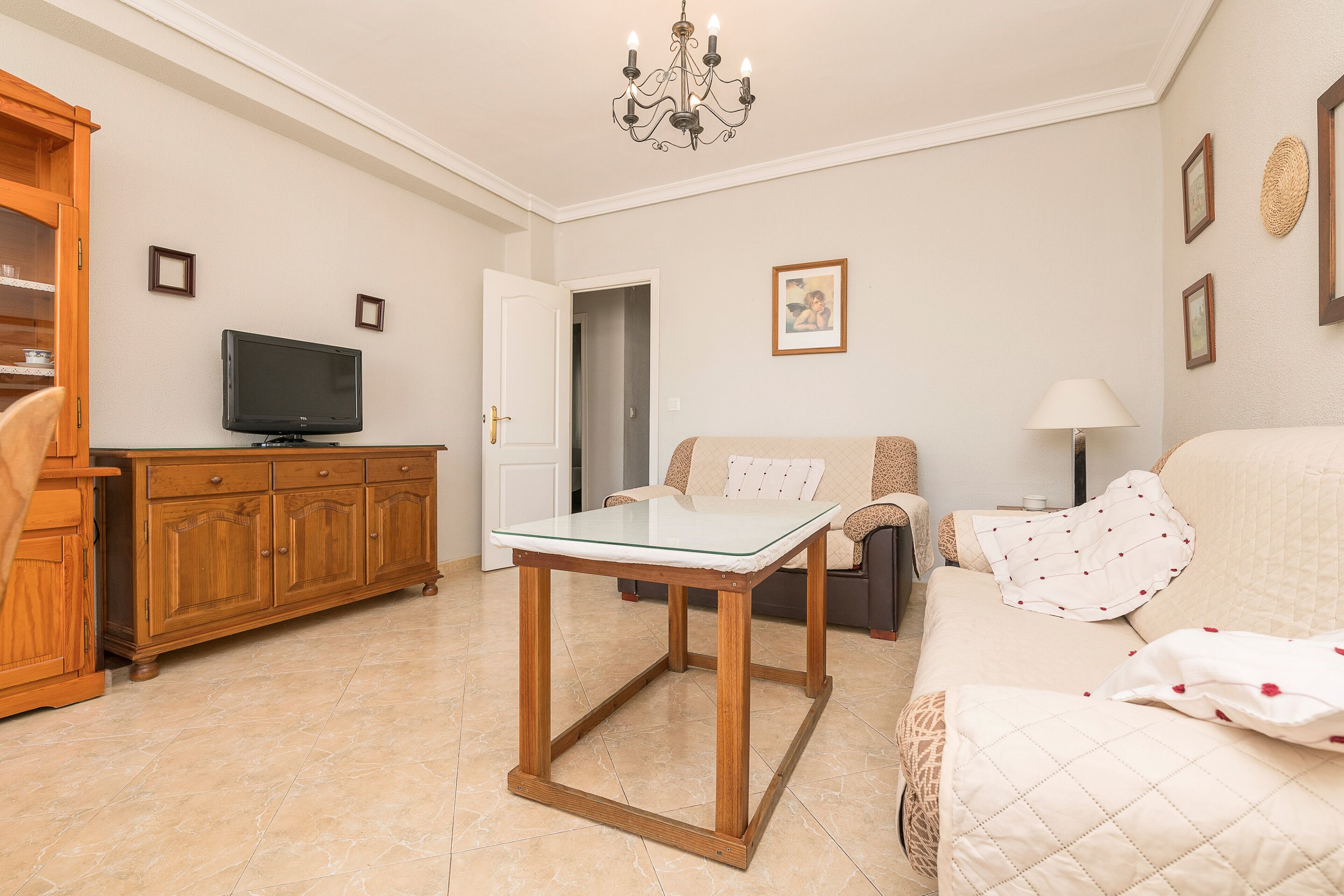 Una sala de estar con una mesa de vidrio, un mueble de madera, un sofá y un televisor.