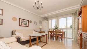 A spacious living room with a sofa, a dining table, and a kitchen area. - PLAYAMAR - Nice flat near the sea in Cadiz and Free WiFi (Cádiz)