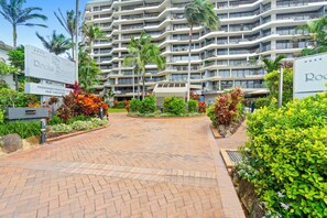 Un hotel de varios pisos con una entrada ajardinada que presenta un camino de ladrillo y plantas tropicales.