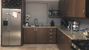 A kitchen with a stainless steel refrigerator, a built-in oven, a gas stove, wooden cabinets, a granite countertop, a ceiling fan, and a window with blinds.