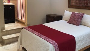 A bedroom with a bed, a nightstand, a bathroom with a sink and mirror, and a staircase leading to an upper floor.