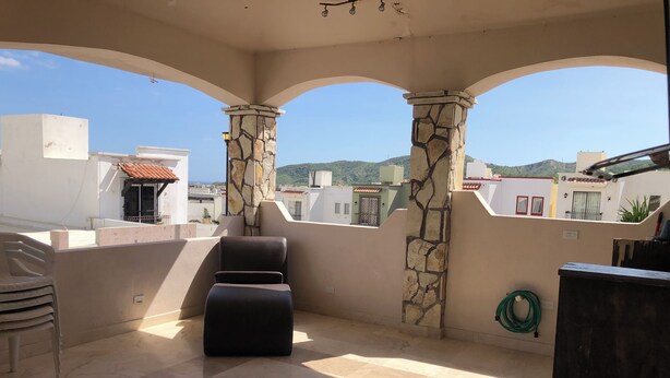 A covered outdoor area with stone pillars, a black lounge chair, and a view of surrounding buildings.