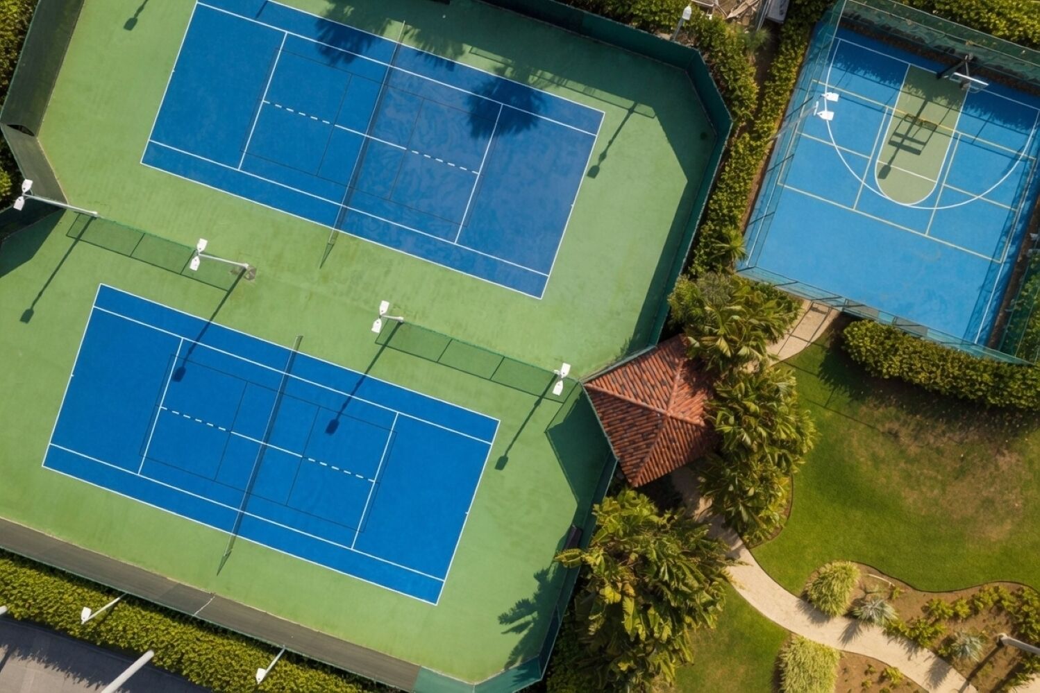 An aerial view of a tennis court complex with multiple courts, surrounded by greenery and a small building.