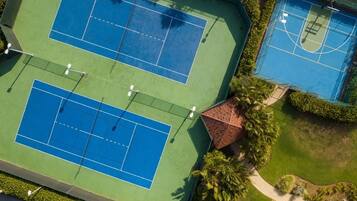 An aerial view of a tennis court complex with multiple courts, surrounded by greenery and a small building.