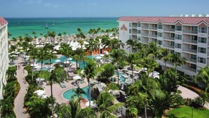 A resort with a pool area, palm trees, and a view of the ocean. - Palm Beach Aruba | Couples Caribbean Getaway | Pool + Beach (Palm Beach)