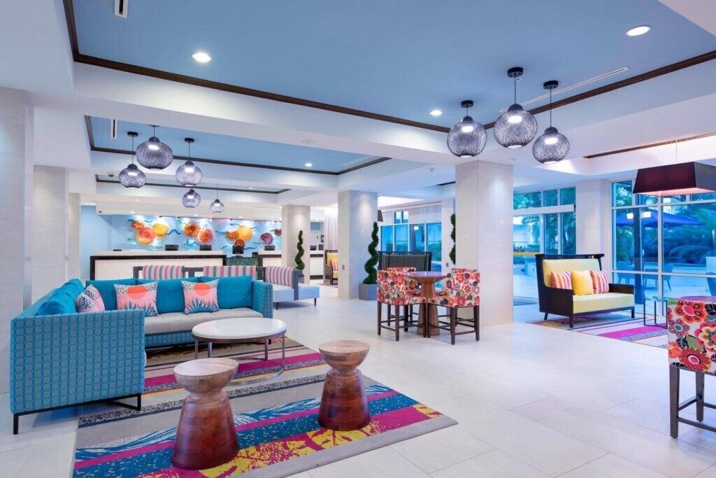 Een moderne hotellobby met een bank, stoelen, een bijzettafeltje en hanglampen.