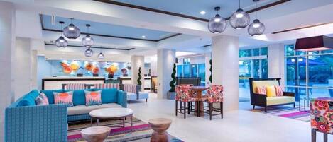 Een moderne hotellobby met een bank, stoelen, een bijzettafeltje en hanglampen.