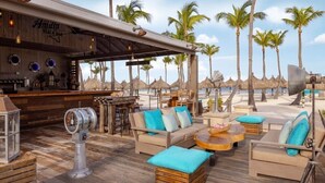 A beach bar with wooden furniture, palm trees, and a view of the beach. - Palm Beach Aruba | Couples Caribbean Getaway | Pool + Beach (Palm Beach)