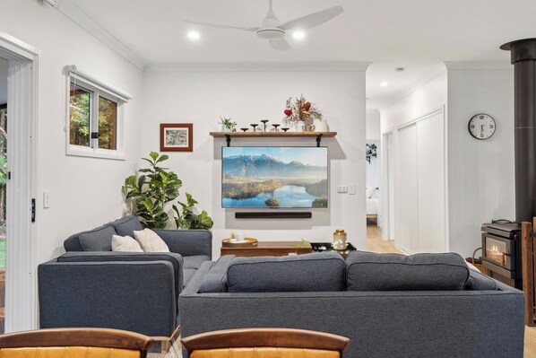 A modern living room with a grey sofa, a flat-screen TV mounted on the wall, a ceiling fan, and a fireplace.