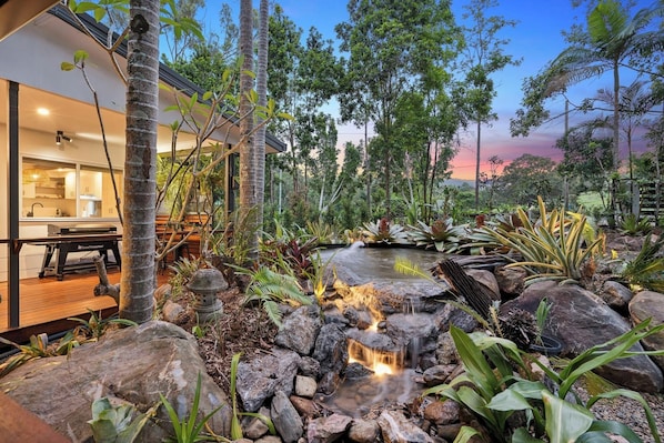 Una casa moderna con cocina, comedor y jardín con una pequeña cascada.